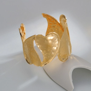 Gold wide cuff bracelet with heart cutouts and hammered texture on white stand