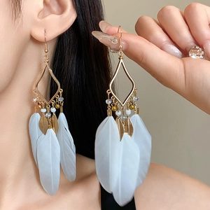 Detail of bohemian gold leaf earrings with white feathers and rhombus metal design