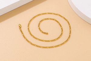 Detailed view of a golden Figaro chain necklace with interlocking metal links on beige surface