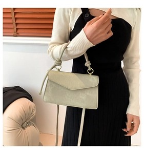 Détail du sac à main vert sauge avec finitions dorées et poignée à nœud décoratif