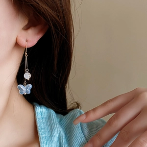 Detail of long gold earrings featuring blue butterfly charms and white round beads