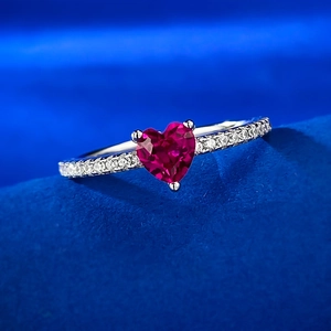 Macro shot of heart-cut red ruby ring with silver pavé band on dark blue velvet