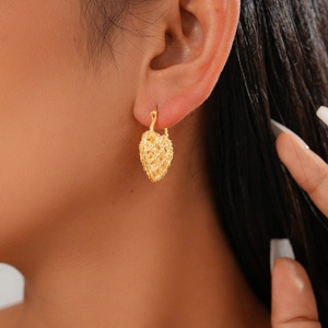 Close-up of a model wearing a gold hollow heart hoop earring with woven metal texture