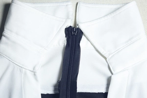Dettaglio del colletto di un body bianco con cerniera scura e trama in maglia fine