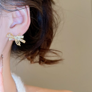 Macro shot of gold-plated bow earrings with cubic zirconia worn on a model ear