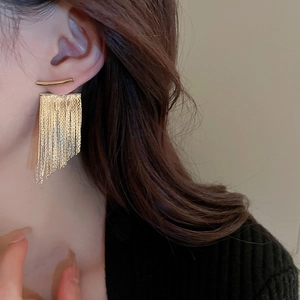 Close-up of golden long tassel drop earring worn by a model in a minimalist French style