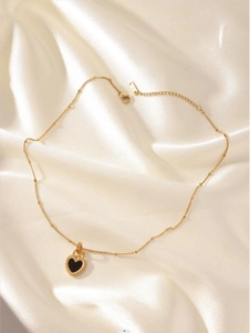 Close-up of gold beaded chain with black heart pendant on white silk background