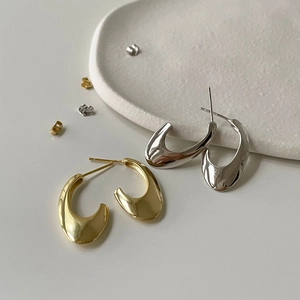 Detailed view of minimalist U-shaped gold and silver earrings on a ceramic tray