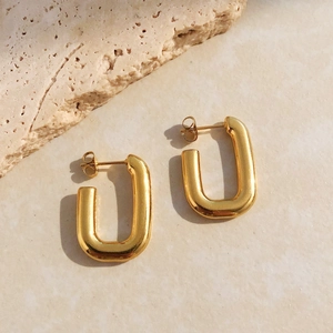 Vue détaillée de boucles d'oreilles en U en acier plaqué or sur un fond en pierre