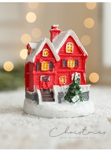 Close-up of red resin Christmas cottage with snow and a miniature green pine tree