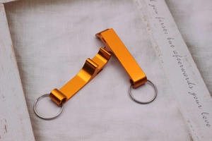 Close-up of two orange metal keychain bottle openers on white fabric with wooden decor