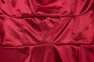Detail of red satin dress featuring corsetry boning structure and glossy fabric texture
