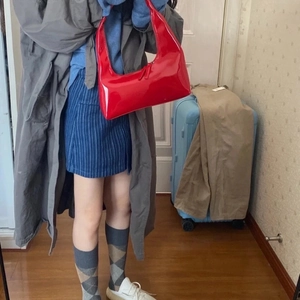 Retro red glossy patent leather crescent shoulder bag held by a model in a home setting