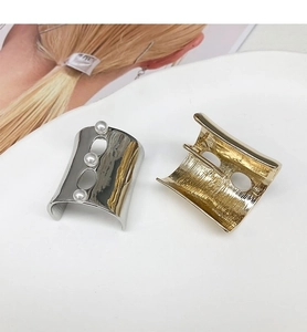 Detail of U-shaped gold textured hair pin and silver pearl hair clip on white plate