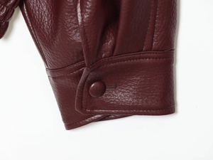 Detail of burgundy faux leather jacket cuff with visible lychee texture and button closure