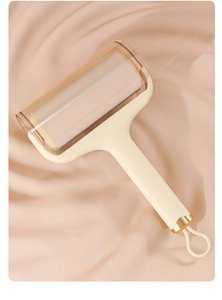Detail view of cream ergonomic lint roller with translucent dust cover on silk background