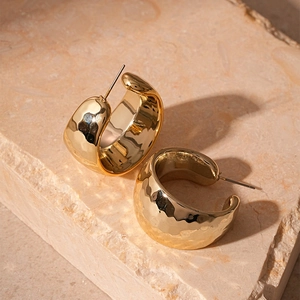 Detailed view of golden C-shaped hoop earrings with hammered metal texture and steel pins