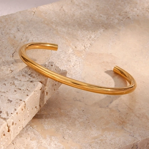 Minimalist gold plated stainless steel open bangle displayed on a natural stone base