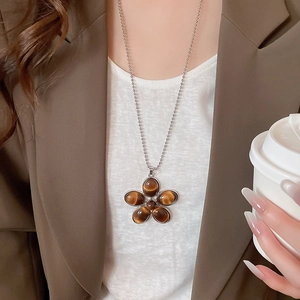 Close-up of a resin floral pendant necklace with tiger eye stones worn with a blazer