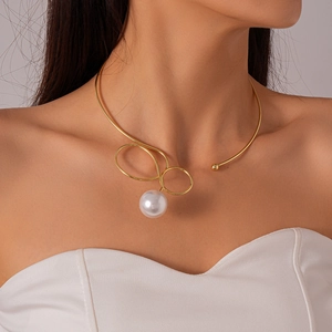 Detail of a gold metallic collar necklace featuring a round pearl on a model's collarbone