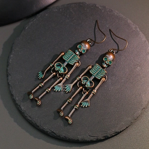 Gothic skull drop earrings with vintage green patina finish on a dark slate stone base