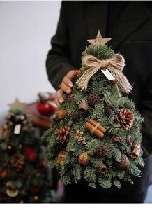 Mini DIY Christmas tree with pine cones, cinnamon sticks, and star details held by hand