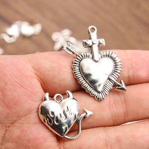 Macro detail of silver heart charms with devil horns and cross accents held in hand