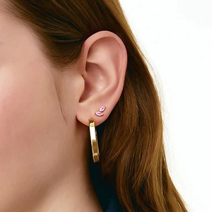 Detail of leaf-shaped pink stone stud and flat gold hoop earrings on model
