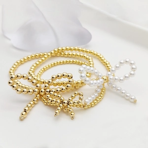 Three-piece gold beaded bracelet set with elegant white pearl bow charm accents
