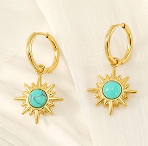 Close-up of gold hoop earrings with turquoise starburst pendants on white fabric