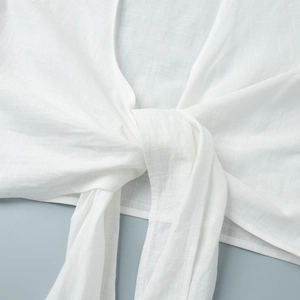 Detail of white puff sleeve tie-front top showing natural linen texture and bow knot