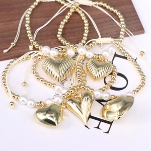 Detail showing golden heart pendants and pearl beads on woven adjustable bracelets