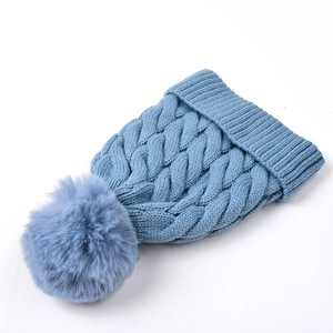 Close-up of blue cable-knit winter hat featuring a large fluffy pom-pom on white background
