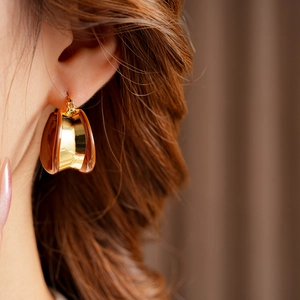 Gros plan sur des boucles d'oreilles créoles dorées avec émail ambre sur modèle