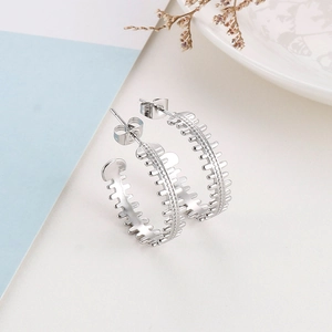Macro detail of silver C-shaped geometric hoop earrings with industrial gear pattern