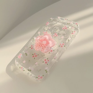 Clear iPhone case featuring pink floral patterns and a 3D flower grip with pearl detail