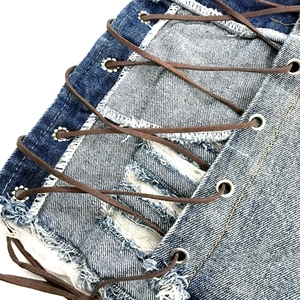 Dettaglio di pantaloncini in denim con lacci laterali in pelle e occhielli in metallo argento