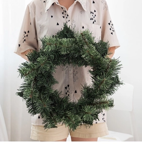 Nahaufnahme eines üppigen grünen künstlichen Kiefernnadel-Weihnachtskranzes in der Hand