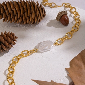 Détail d'un collier en chaîne dorée avec perle baroque sur fond de pierre blanche texturée