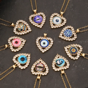 Golden heart pendants with cubic zirconia and evil eye designs on stone background