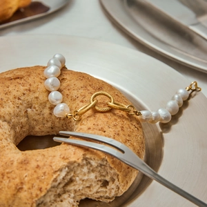 Artistic close-up of a 18K gold-plated pearl bracelet with OT buckle on a silver tray