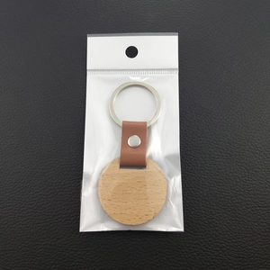 Minimalist round wooden keychain with brown leather strap and metal ring in packaging