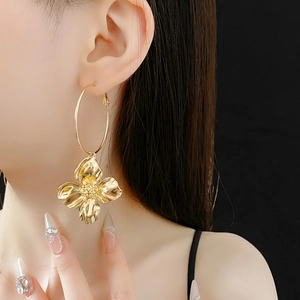 Close-up of model wearing large gold hoop earrings with flower pendant on black background