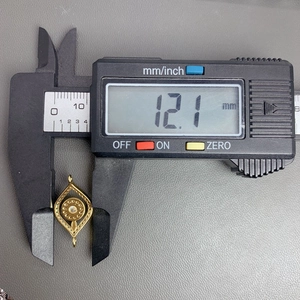 Caliper measuring a 12.1mm gold evil eye pendant with a white zircon center stone