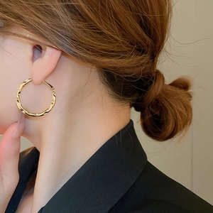 Detail of irregular textured gold hoop earrings on model with high gloss finish