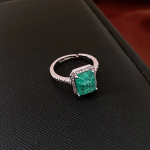 Detail of silver ring with green emerald-cut zircon surrounded by white stones