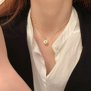 Detail of a gold circular medallion necklace with a rose relief worn by a model