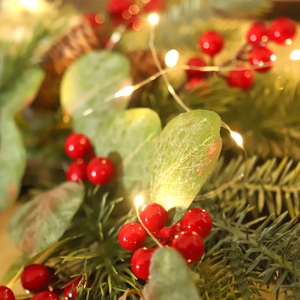 Christmas wreath with red berries, green foliage and warm LED fairy lights on front door