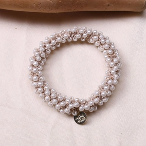 Detail of beaded pearl hair tie with gold 'Hand Made' charm on elegant satin fabric