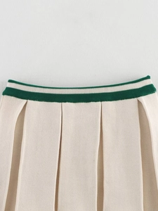 Detailed close-up of cream knit pleated skirt featuring a contrast green striped waistband